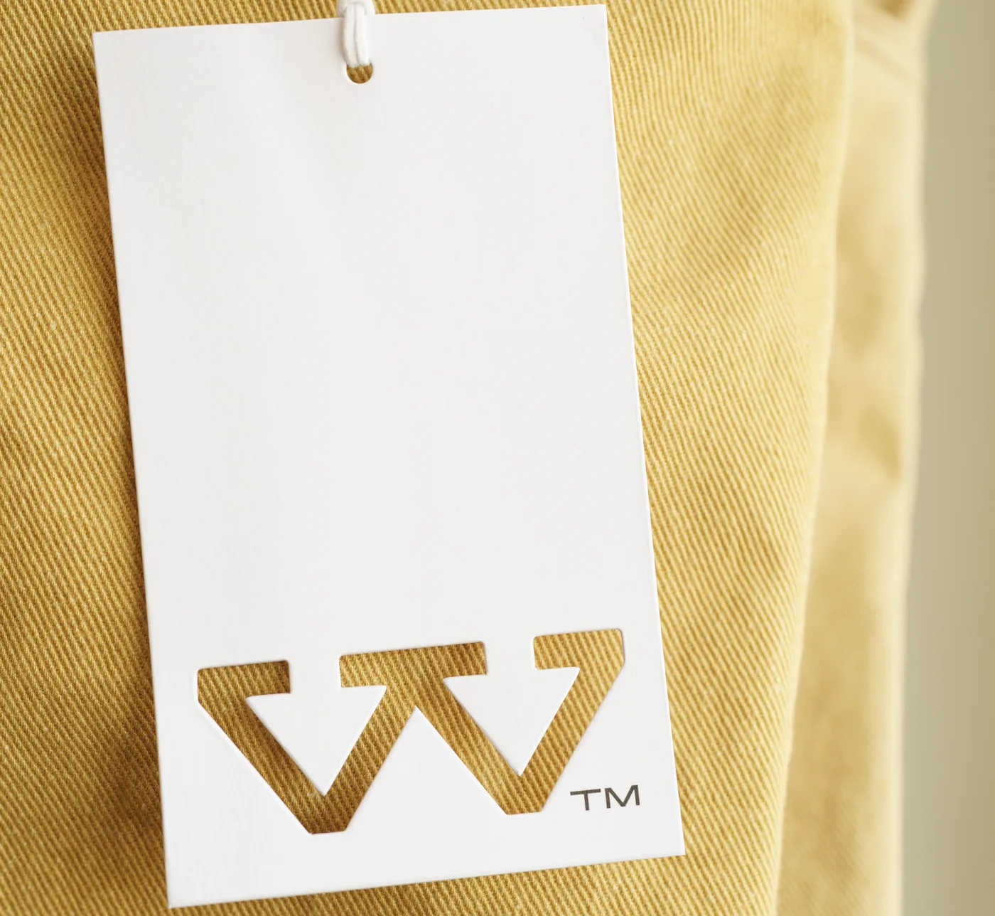 Die-cut WTRLSS W hang-tag over gold-khaki twill