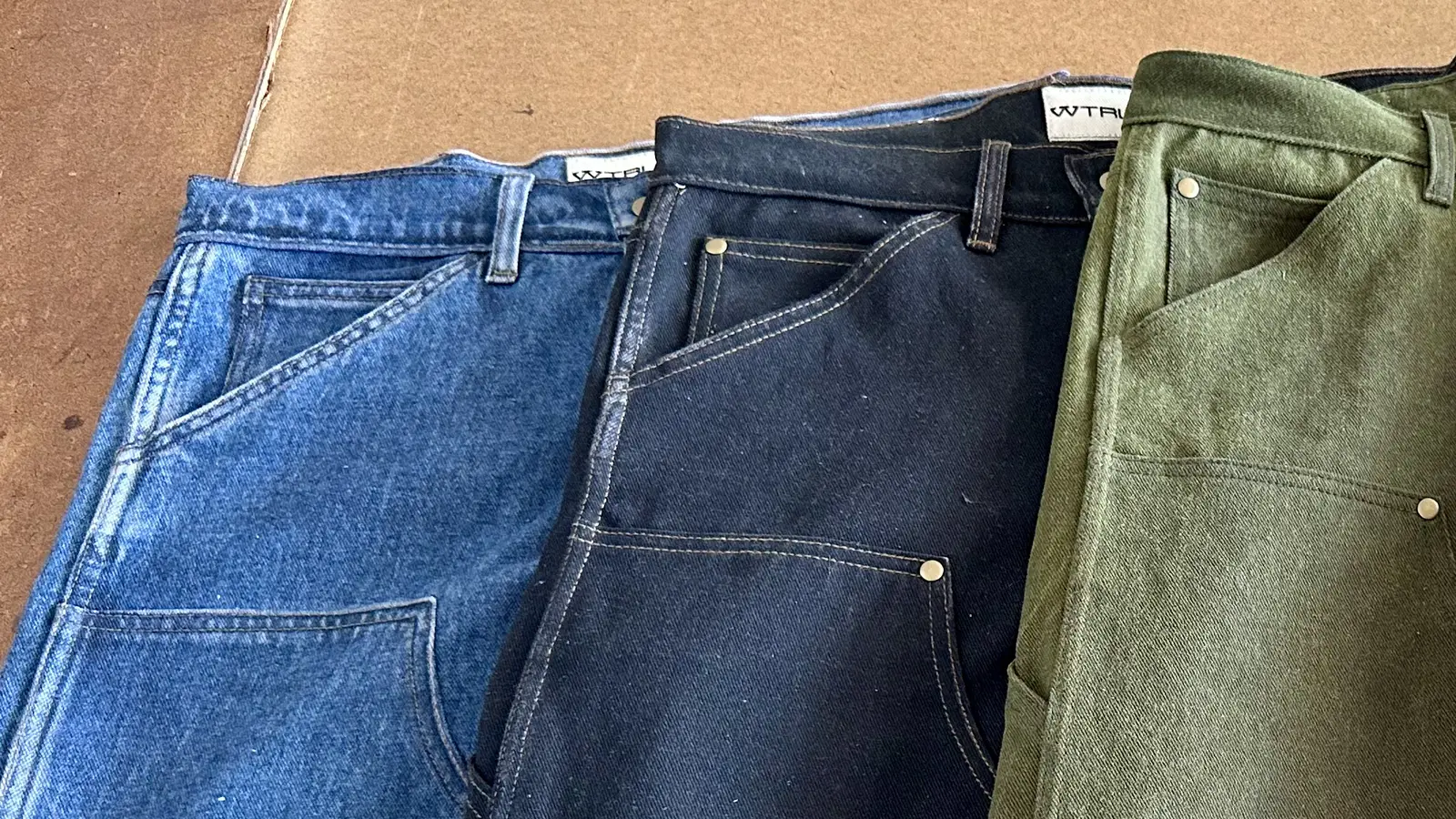 WTRLSS-dyed pants in blue, black, and olive, laid side by side with W hangtags