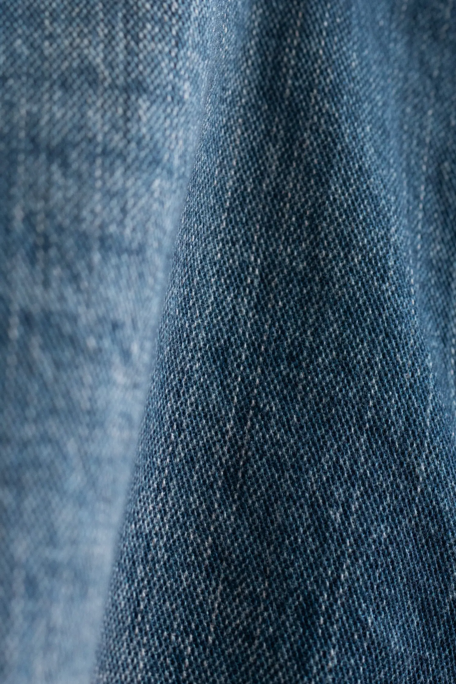 Extreme macro of WTRLSS-dyed indigo denim — white yarn cores showing through the surface, the ring-dye effect